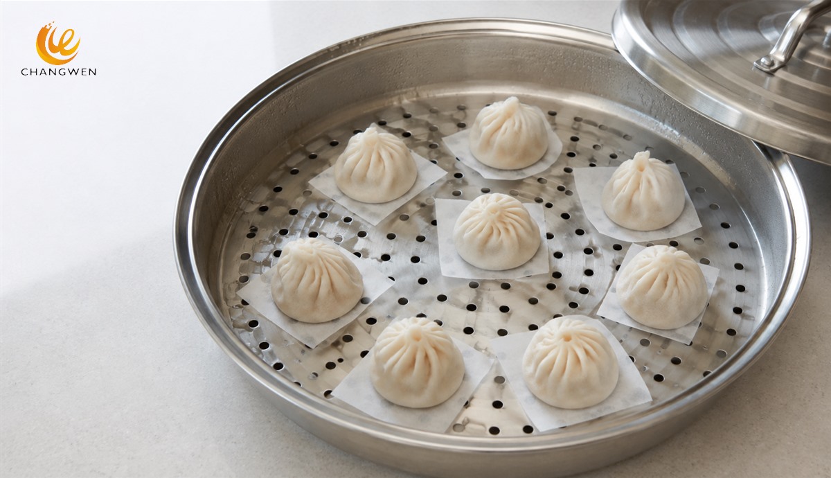 Dumplings arranged with visible gaps on a perforated stainless steel steamer tray